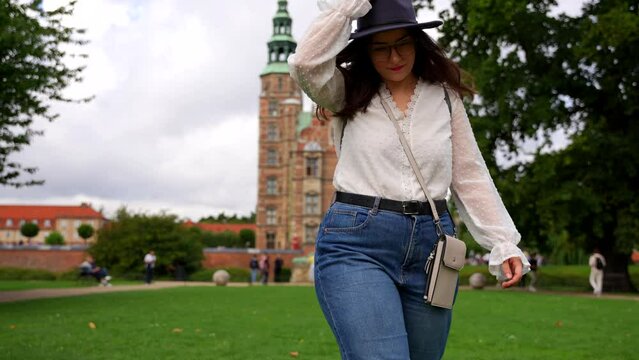 Woman with casual clothes and hat walks towards camera near Rosenborg Castle