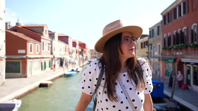 Female tourist with hat enjoys sun on bridge over Canal in Murano, Italy