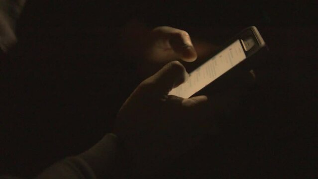 close up of a black mans hands scrolling his phone in the dark