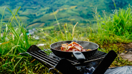 Camping breakfast with bacon in a cast iron skillet. Fried bacon in a pan in the forest. Food at...