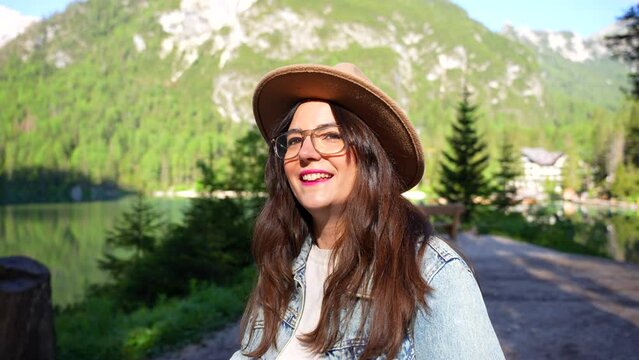 Woman with brown hat turns and smiles at camera in Lago di Braies forested area, Italy