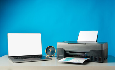 Modern printer with paper and laptop on table in office