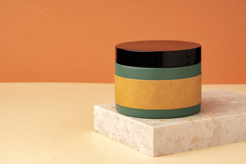 Cosmetic jar and stone on brown background