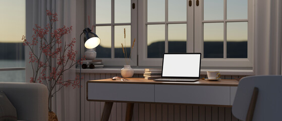 A laptop mockup on a table in a modern living room in the evening with light from a floor lamp.