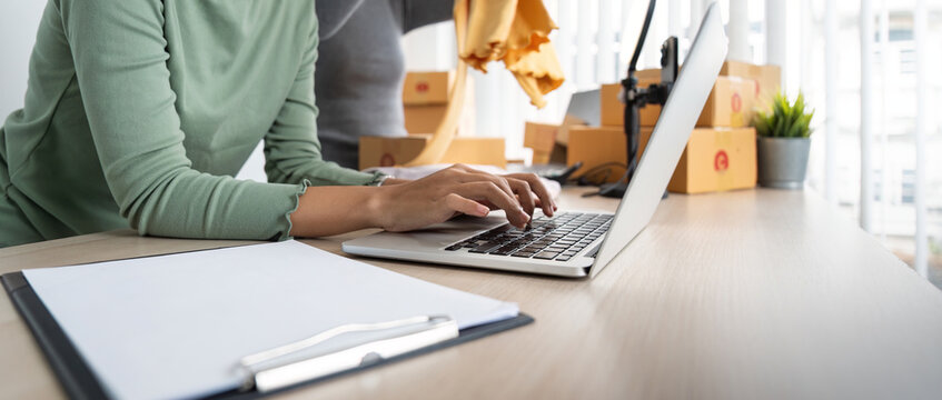 Startup Small Business Owner Working With Computer At Workplace. Two Woman Seller Check Product Order. Packing Goods For Delivery To Customer. Online Selling. Ecommerce. Online Shopping