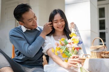 Obraz na płótnie Canvas Happy Asian couple enjoying picnic together. A boyfriend surprise his girlfriend with flowers.