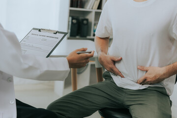 Crohn's disease or ulcerative colitis concept. Doctor counseling male patient with abdominal pain in hospital examination room - obrazy, fototapety, plakaty