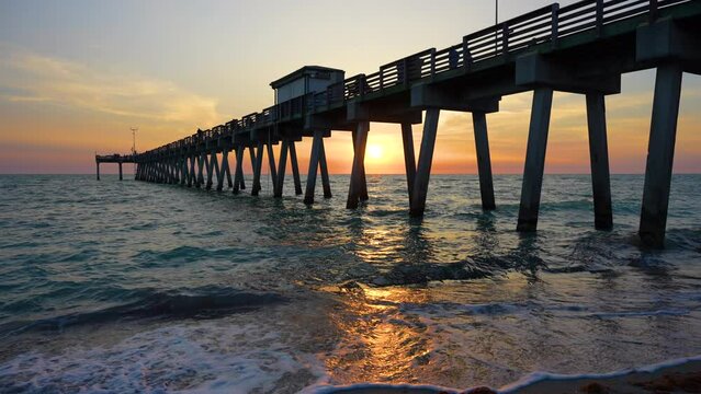 Sunset landscape at Venice fishing pier in Florida. Ocean surf waves crashing on sandy beach covered with sargassum seaweed