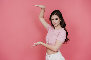Brunette caucasian girl standing against pink studio background holds by hand  imaginable product,...