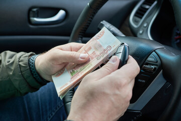 Hands of a man driving a car with money and keys in hand. Concept - buying a car.