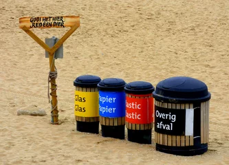 Fototapeten Four rubbish bins to separate waste on the beach. They are labeled in Dutch: glass, paper, plastic, other waste. On pole is written: throw it here, save an animal (gooi het hier, red een dier) © Wolfborn Indiearts