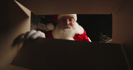 Santa Claus putting toy into cardboard box and closing close-up, wrapping gifts for kids. Christmas...