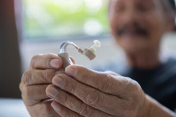 Happy man at home with hearing aid finally hears. Portrait of smiling senior man holding ear with satisfaction looking at it. - obrazy, fototapety, plakaty