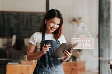 Happy excited attractive young Asian woman in denim apron, received online order in coffee shop...