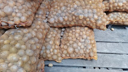 The portrait of a stack of potato seeds inside an orange sack on top of a wooden pallet
