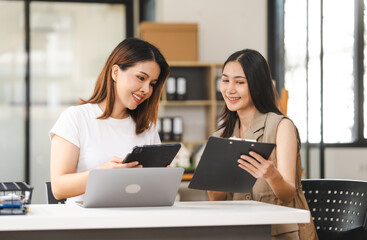 Two Asian colleagues, freelance writer and graphic designer discussing about creating characters in screenplays work and smiling with tablets and a laptop, journalist, artist, meeting together