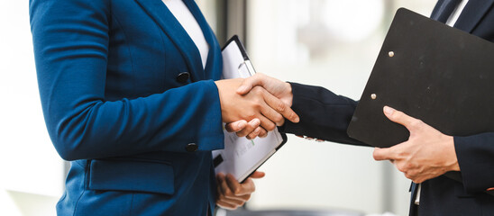 Two middle aged and young Asian business woman in formal suits are shaking hands in an office,...