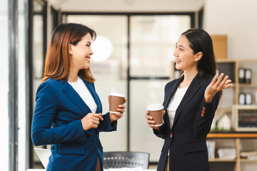 Two middle aged and young Asian female executives in formal suits review bar chart, discussing business strategies in office setting, senior executives or directors in advertising or public relations
