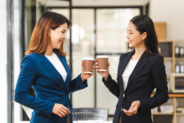 Two middle aged and young Asian female executives in formal suits review bar chart, discussing business strategies in office setting, senior executives or directors in advertising or public relations