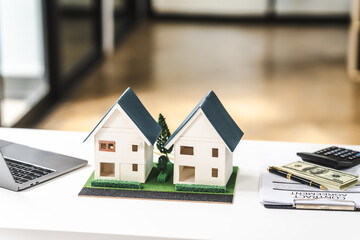 Two model houses on a desk with a laptop and paperwork, representing real estate property for sale or investment.