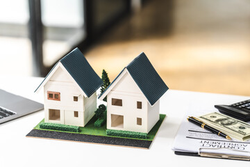 Two model houses on a desk with a laptop and paperwork, representing real estate property for sale or investment. - obrazy, fototapety, plakaty