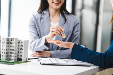 Two middle aged and young Asian business woman in formal suits discuss over model buildings, on city investment and development strategies. urban investment opportunities in city, condo, apartment.