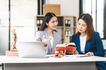 Two middle aged and young Asian lawyer in a formal suit consoles a client during a legal consultation, with a gavel and documents on the table.