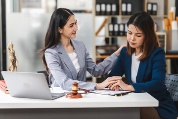 Two middle aged and young Asian lawyer in a formal suit consoles a client during a legal consultation, with a gavel and documents on the table.