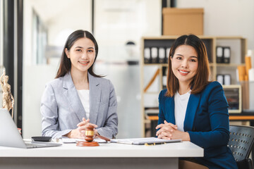 Two middle aged and young Asian lawyer in a formal suit consoles a client during a legal consultation, with a gavel and documents on the table.