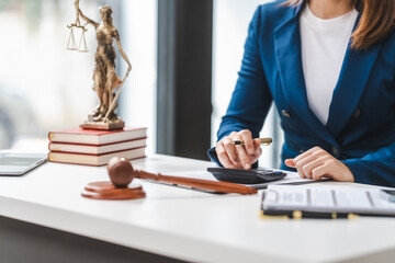 Close up of a lawyer calculating expenses, with a legal contract, gavel, and law books on the table. - obrazy, fototapety, plakaty