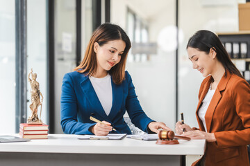 Two young and middle-aged Asian women lawyers in formal suits discuss legal contract, focusing on legislation and women's rights in law office.