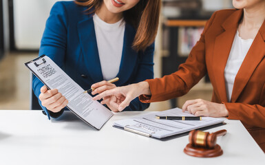 Two young and middle-aged Asian women lawyers in formal suits discuss legal contract, focusing on...
