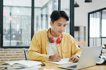 Young collage student using computer and mobile device studying online...