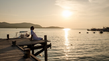 Asian woman watching sunset at a wooden pier in the ocean during sunset in Samaesan Thailand