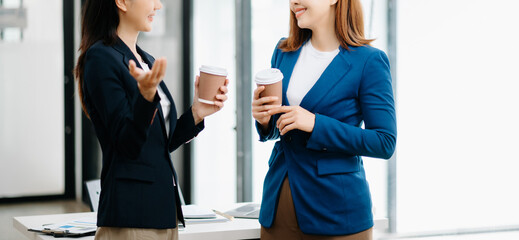 Happy two Asian business woman holding coffee cup in moderm office