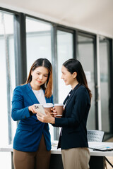 Obraz premium Happy two Asian business woman holding coffee cup in moderm office