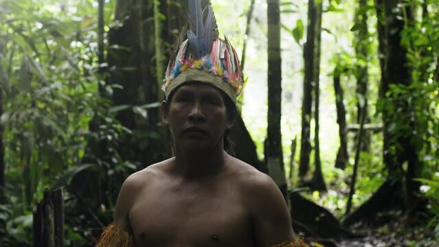 An indigenous guy wearing a feathered hat and fringed shirt in the dense forest in Leticia, Amazon, Colombia