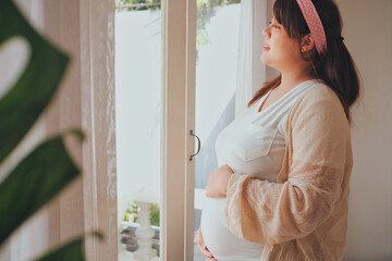 Asian young pregnant woman touching her belly at home.