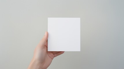 Blank white square greeting card opened by female hand with manicured nails. Mockup. Top view....