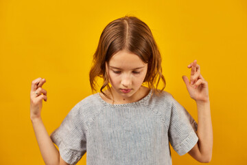 Teen girl fingers crossed on yellow studio background