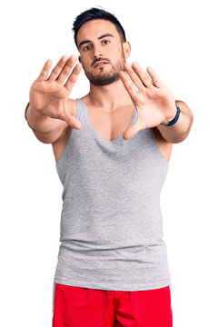 Young handsome man wearing swimwear and sleeveless t-shirt doing frame using hands palms and fingers, camera perspective