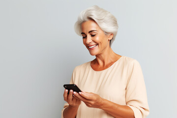 Matured woman looking at smart phone in her hand & isolated on minimalist gray background. beautiful smiling woman with good health holding phone on hand. Short hair modern 50s mid-aged woman portrait
