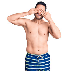 Fototapeta premium Young handsome man wearing swimwear covering eyes with hands smiling cheerful and funny. blind concept.