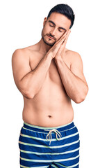 Fototapeta premium Young handsome man wearing swimwear sleeping tired dreaming and posing with hands together while smiling with closed eyes.