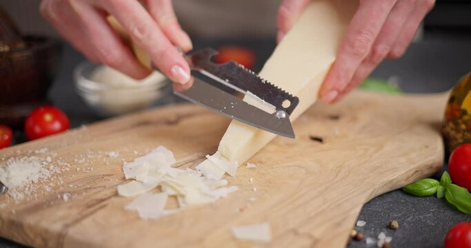 Woman slicing Piece of Traditional Italian Parmesan Hard cheese into flakes on a wooden cutting board at domestic kitchen