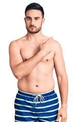 Fototapeta premium Young handsome man wearing swimwear pointing with hand finger to the side showing advertisement, serious and calm face
