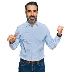 Middle aged man with beard wearing business shirt pointing to the back behind with hand and thumbs...