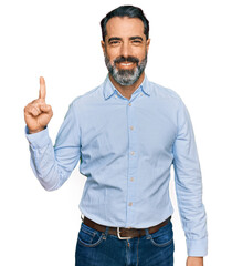Naklejka premium Middle aged man with beard wearing business shirt showing and pointing up with finger number one while smiling confident and happy.