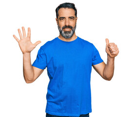 Middle aged man with beard wearing casual blue t shirt showing and pointing up with fingers number six while smiling confident and happy.