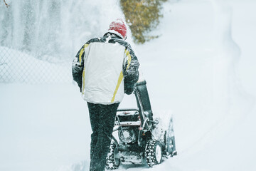 Man removes snow with a snowblower rear view. working with a gasoline snow blower after the severe...